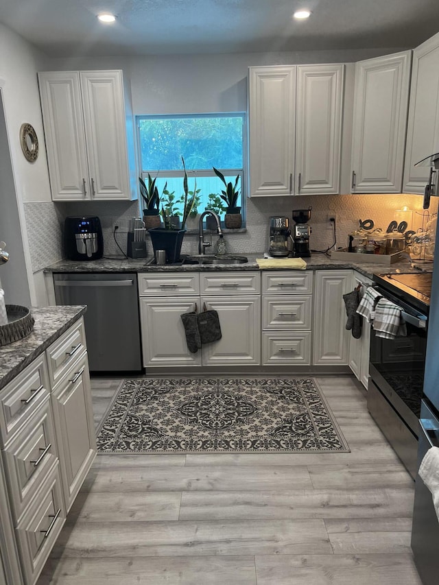 kitchen featuring stainless steel appliances, dark stone counters, white cabinets, light wood-type flooring, and sink