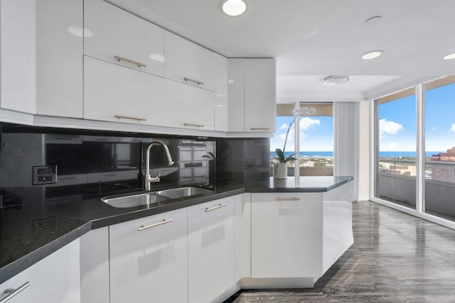 kitchen featuring tasteful backsplash, white cabinets, sink, and a water view