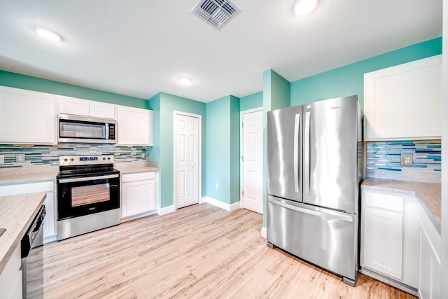 kitchen with white cabinets, appliances with stainless steel finishes, light hardwood / wood-style floors, and tasteful backsplash