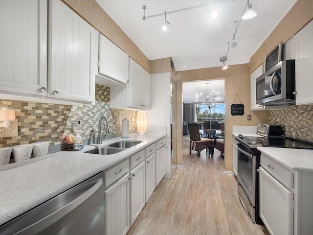 kitchen with light wood-type flooring, sink, white cabinetry, appliances with stainless steel finishes, and decorative light fixtures