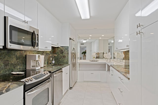 kitchen featuring appliances with stainless steel finishes, dark stone countertops, white cabinets, light tile floors, and tasteful backsplash