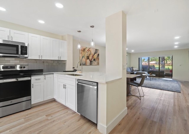 kitchen with appliances with stainless steel finishes, decorative light fixtures, sink, white cabinets, and light wood-type flooring