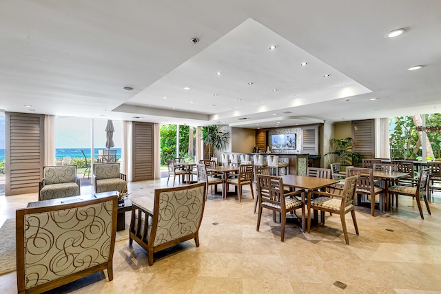 dining area featuring a water view, a tray ceiling, and light tile floors