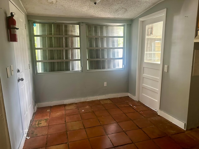 unfurnished dining area featuring a textured ceiling, dark tile patterned flooring, and lofted ceiling