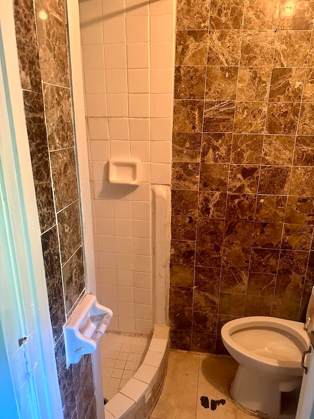 bathroom with tile walls, tiled shower, toilet, and tile patterned flooring