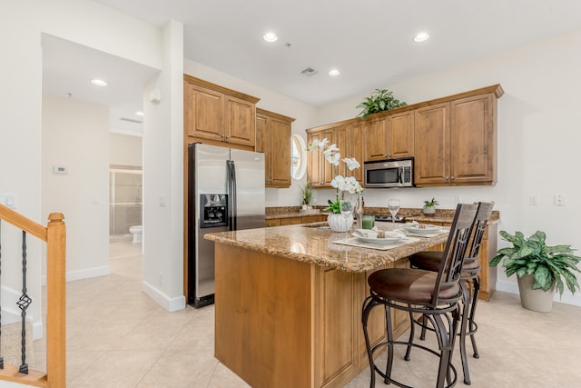 kitchen with light tile flooring, a kitchen bar, stainless steel appliances, light stone counters, and a kitchen island