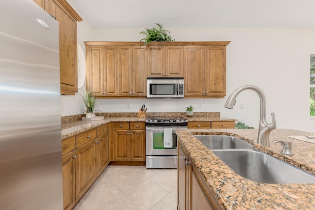 kitchen featuring stainless steel appliances, sink, light tile floors, and light stone counters