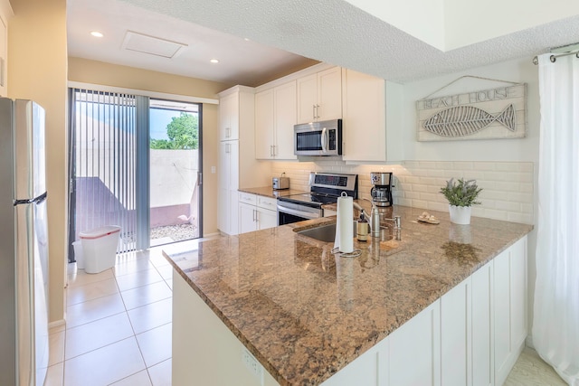 kitchen with tasteful backsplash, kitchen peninsula, stone countertops, and appliances with stainless steel finishes