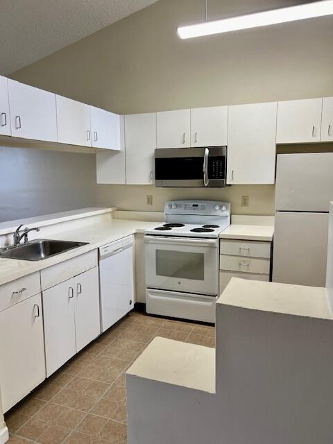 kitchen with white cabinetry, white appliances, sink, and lofted ceiling