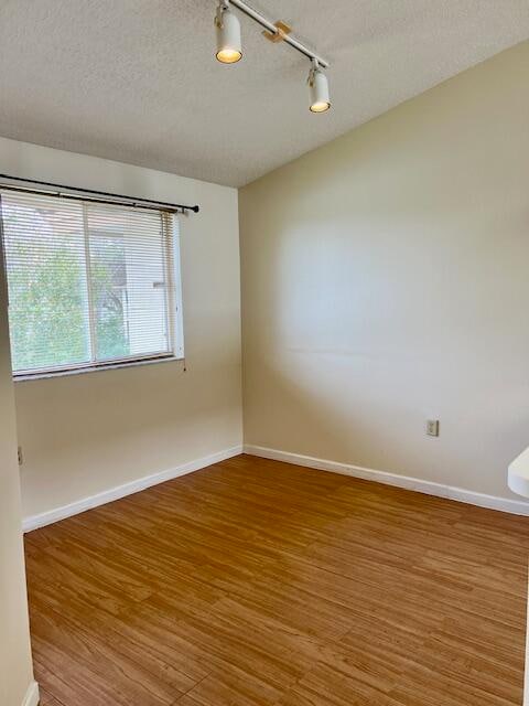 empty room featuring track lighting, hardwood / wood-style floors, and a textured ceiling