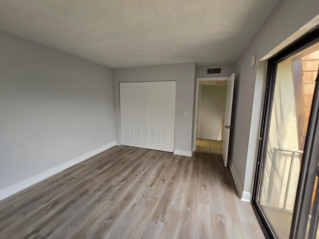 unfurnished bedroom with a textured ceiling, light hardwood / wood-style floors, multiple windows, and a closet