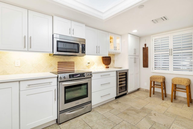 kitchen featuring backsplash, white cabinets, wine cooler, ornamental molding, and stainless steel appliances