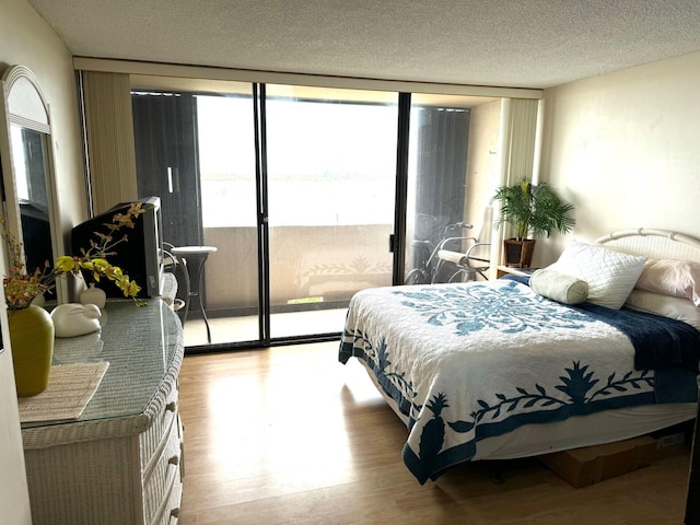 bedroom featuring access to exterior, a textured ceiling, floor to ceiling windows, and light hardwood / wood-style floors