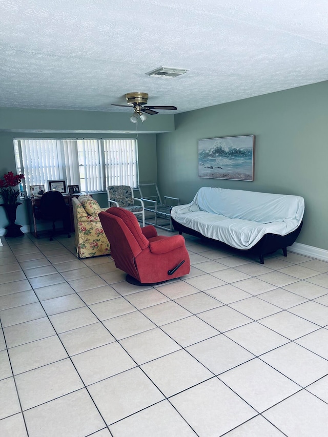 living room with a textured ceiling, ceiling fan, and light tile floors