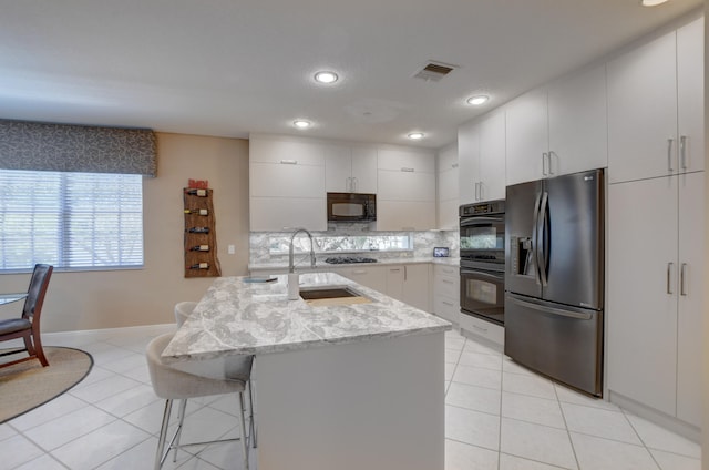 kitchen with an island with sink, light stone counters, black appliances, tasteful backsplash, and white cabinetry