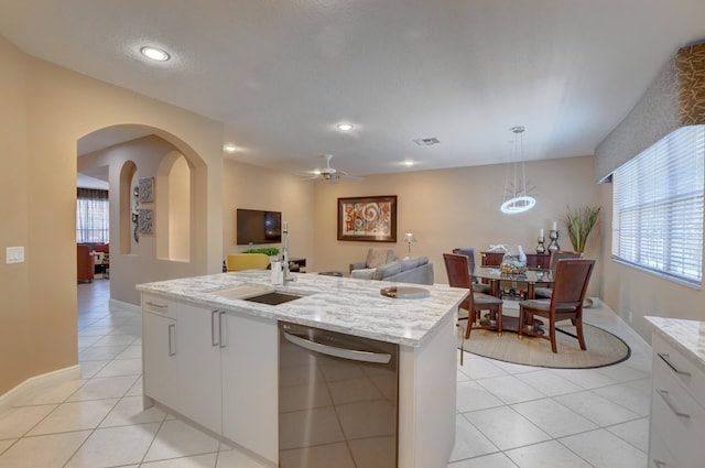 kitchen featuring an island with sink, ceiling fan, pendant lighting, light stone countertops, and white cabinetry