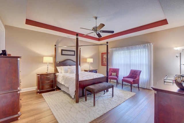 bedroom featuring light hardwood / wood-style floors, a tray ceiling, and ceiling fan