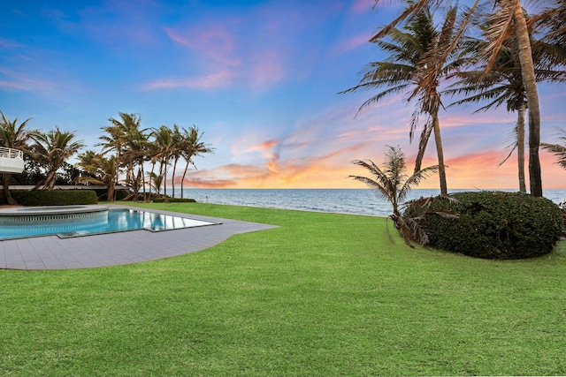 pool at dusk featuring a yard and a water view