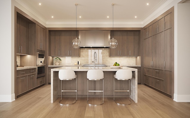 kitchen with wall chimney range hood, ornamental molding, pendant lighting, and light hardwood / wood-style flooring