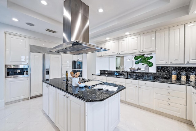 kitchen featuring island range hood, a kitchen island, white cabinetry, backsplash, and a raised ceiling