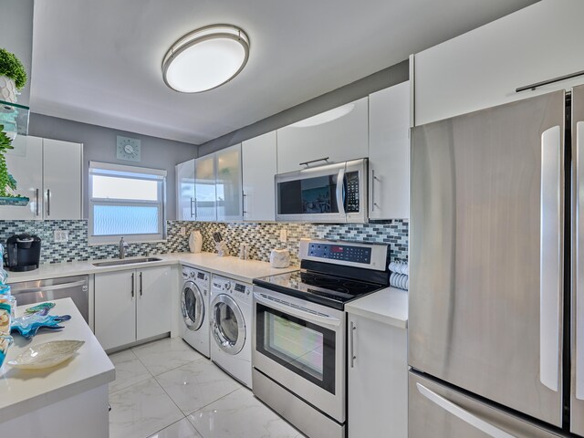 kitchen featuring washing machine and dryer, stainless steel appliances, white cabinets, and sink