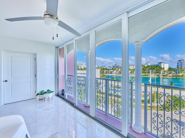 sunroom / solarium featuring decorative columns, ceiling fan, and a water view