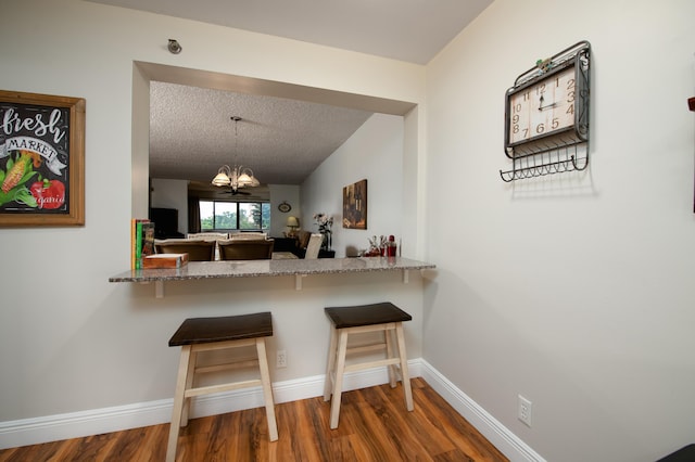 kitchen with baseboards, a breakfast bar, wood finished floors, a notable chandelier, and a textured ceiling