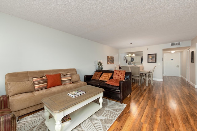 living room featuring a textured ceiling, wood finished floors, visible vents, and a chandelier