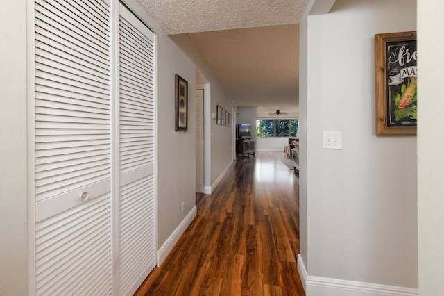 hall featuring dark wood finished floors, baseboards, and a textured ceiling