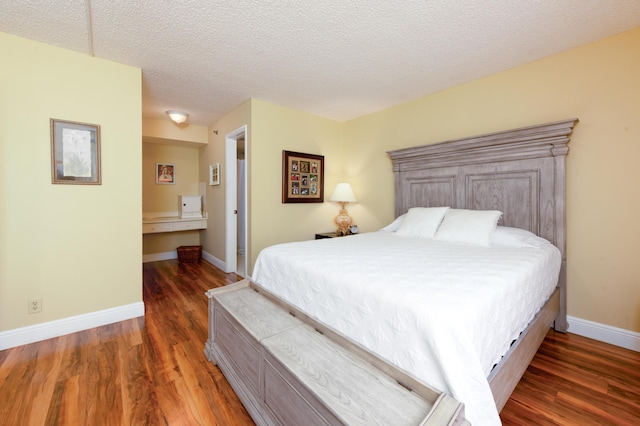 bedroom featuring wood finished floors, baseboards, ensuite bathroom, and a textured ceiling