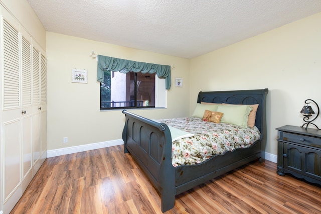 bedroom featuring a closet, baseboards, a textured ceiling, and wood finished floors