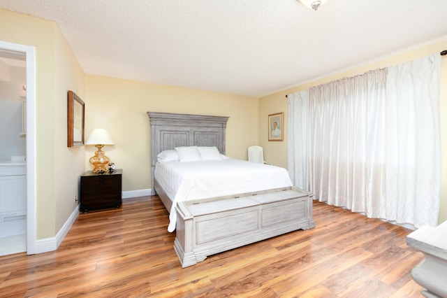 bedroom featuring baseboards, a textured ceiling, light wood-style flooring, and ensuite bathroom