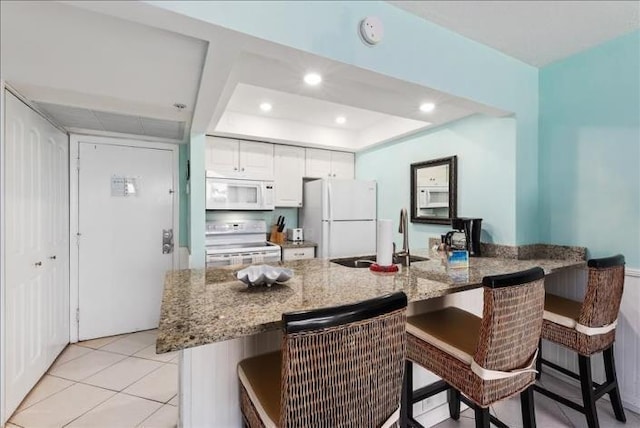 kitchen featuring white appliances, sink, white cabinets, a breakfast bar, and light tile flooring