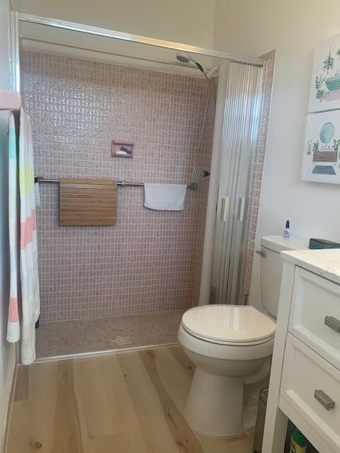 bathroom featuring tiled shower, toilet, vanity, and hardwood / wood-style flooring