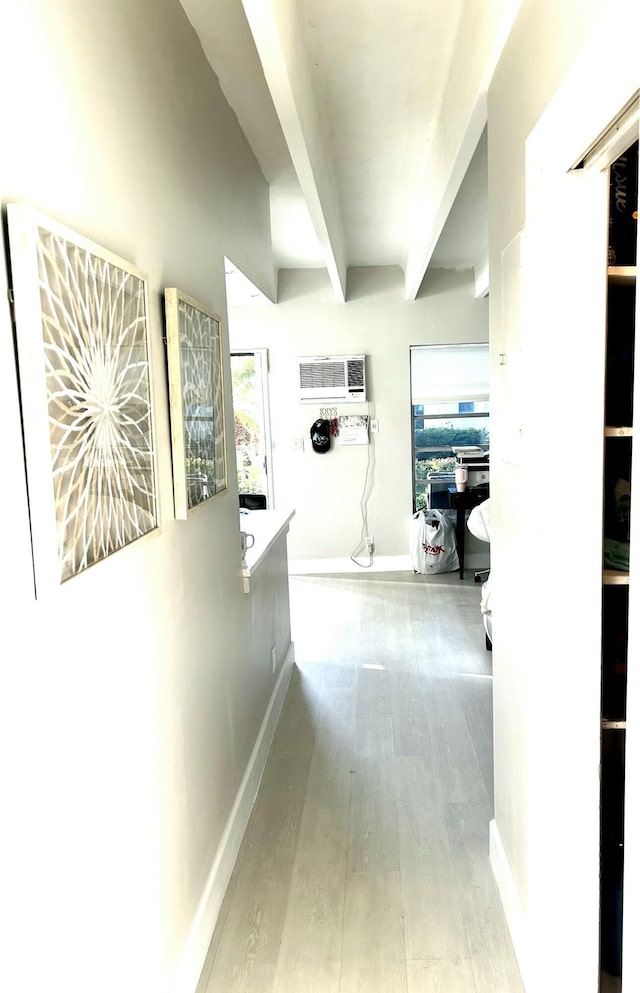 hall with beamed ceiling, light hardwood / wood-style floors, and a wall unit AC