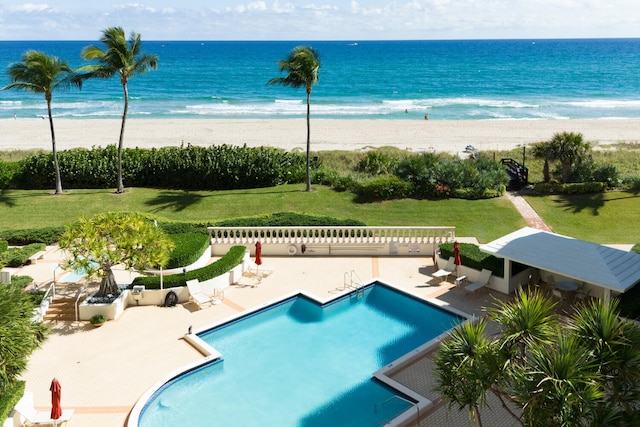 view of swimming pool featuring a lawn, a water view, a patio area, and a beach view