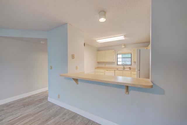 kitchen featuring a kitchen breakfast bar, light hardwood / wood-style floors, white appliances, and a textured ceiling