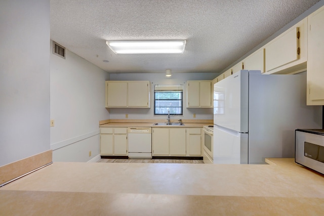 kitchen featuring white appliances, cream cabinets, a textured ceiling, and sink