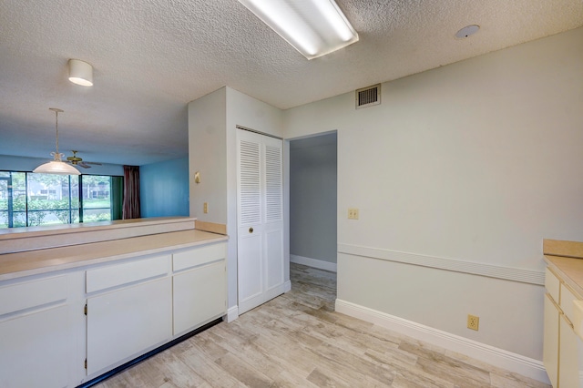 kitchen with ceiling fan, a textured ceiling, white cabinetry, hanging light fixtures, and light wood-type flooring