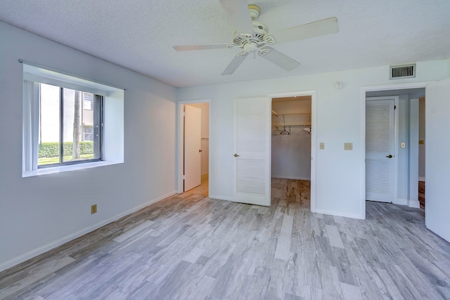 unfurnished bedroom with a spacious closet, ceiling fan, and light hardwood / wood-style flooring