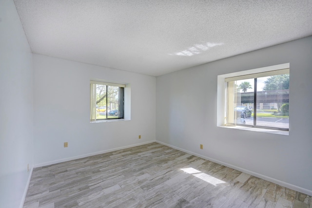 spare room featuring light hardwood / wood-style floors, a textured ceiling, and a wealth of natural light