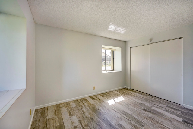 unfurnished bedroom featuring a textured ceiling, a closet, and light hardwood / wood-style flooring