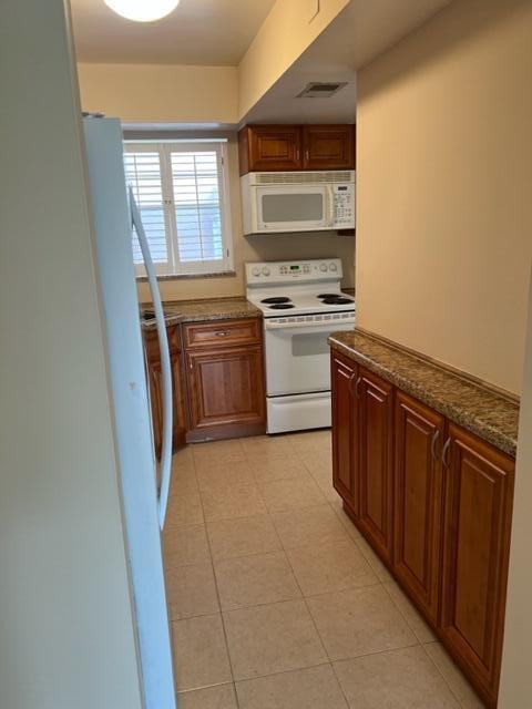 kitchen featuring white appliances, light tile floors, and dark stone counters