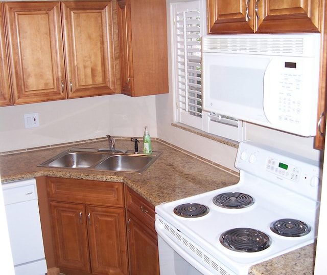 kitchen featuring white appliances, dark stone countertops, and sink