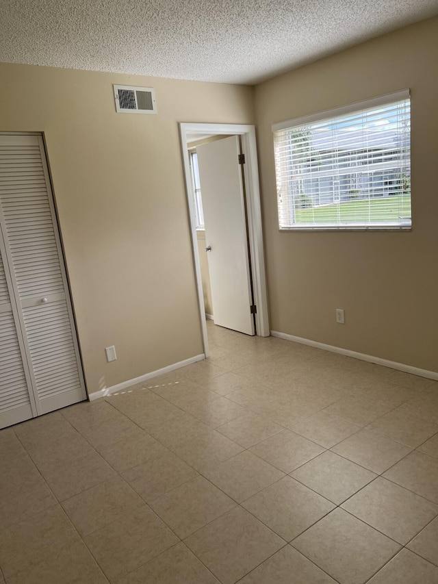 unfurnished bedroom with a closet, a textured ceiling, and light tile floors