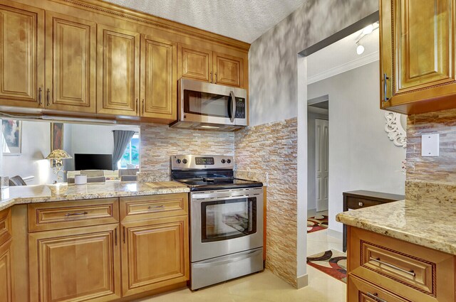 kitchen featuring stainless steel appliances, light tile floors, a textured ceiling, light stone counters, and crown molding