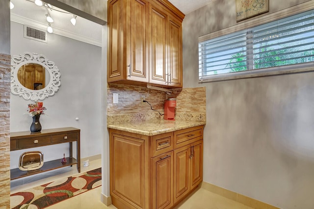 kitchen featuring light stone countertops, track lighting, light tile floors, tasteful backsplash, and crown molding