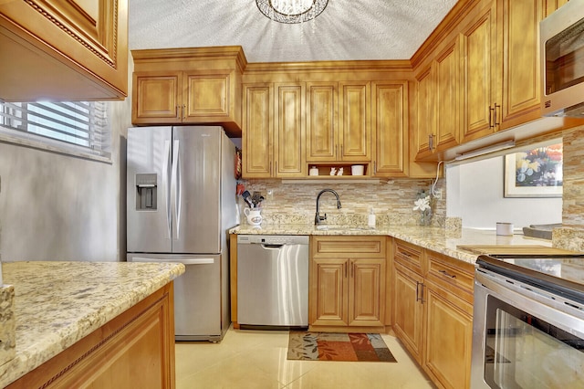 kitchen with light tile flooring, appliances with stainless steel finishes, sink, backsplash, and light stone counters