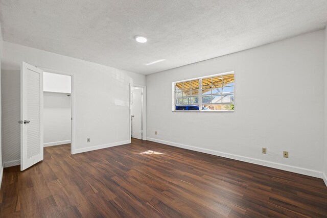 unfurnished bedroom with a spacious closet, dark wood-type flooring, a closet, and a textured ceiling