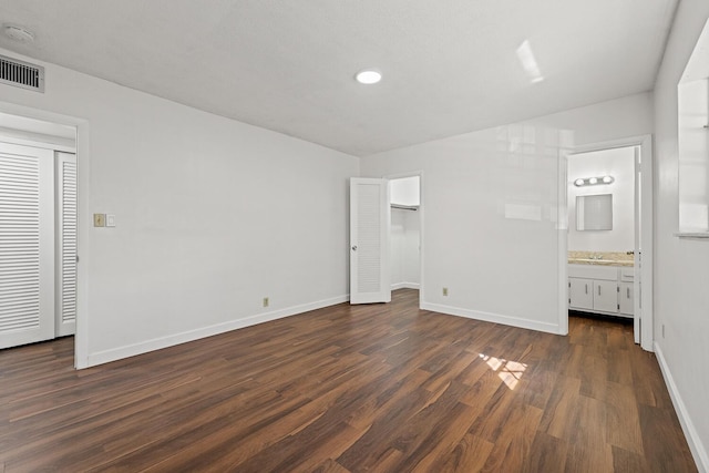 unfurnished bedroom with ensuite bathroom and dark hardwood / wood-style flooring